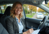 Femme souriante tenant documents d'assurance auto dans sa voiture